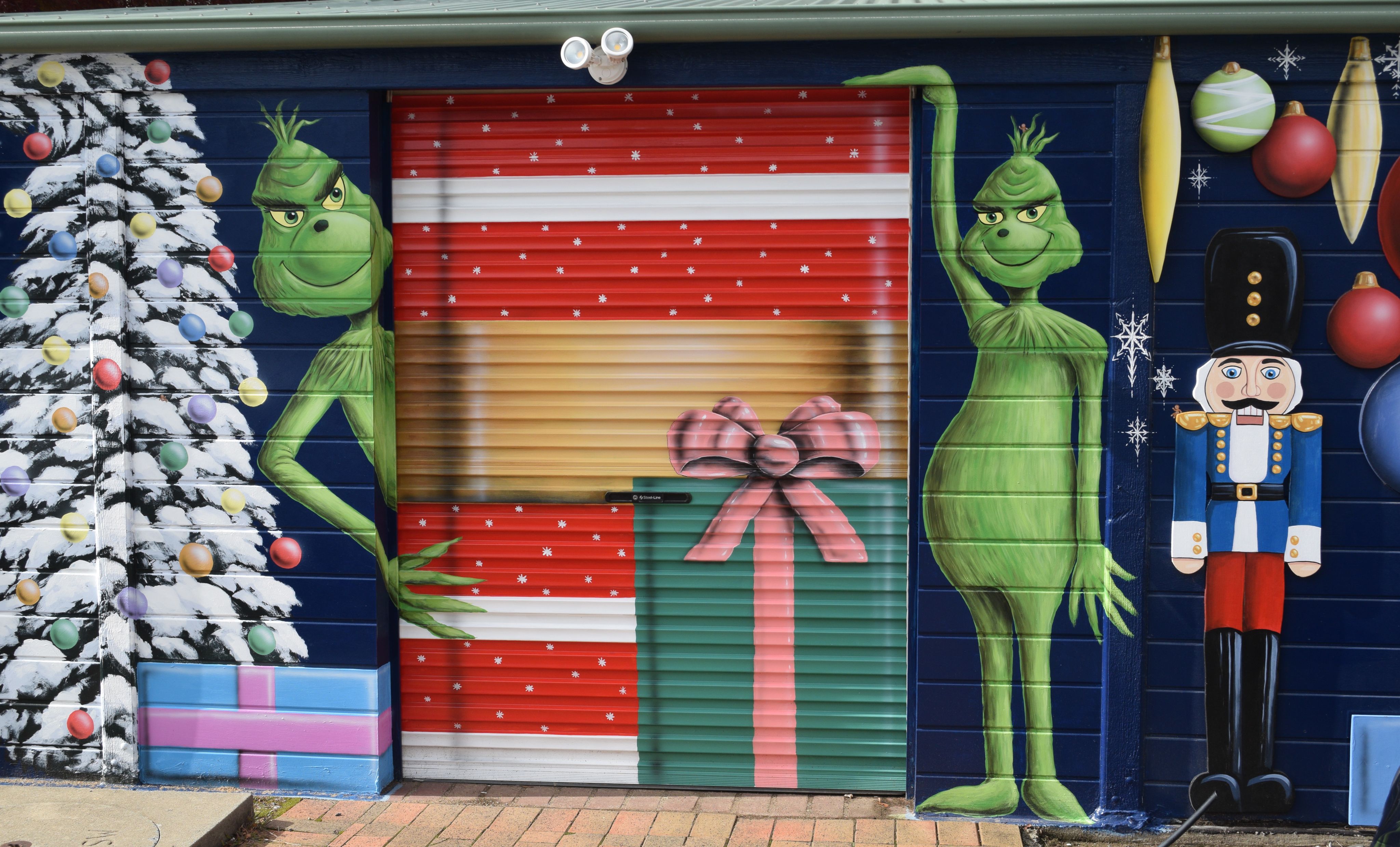 The 'Grinch' mural with 3 large presents, a nut cracker, christmas tree with baubles in the background.