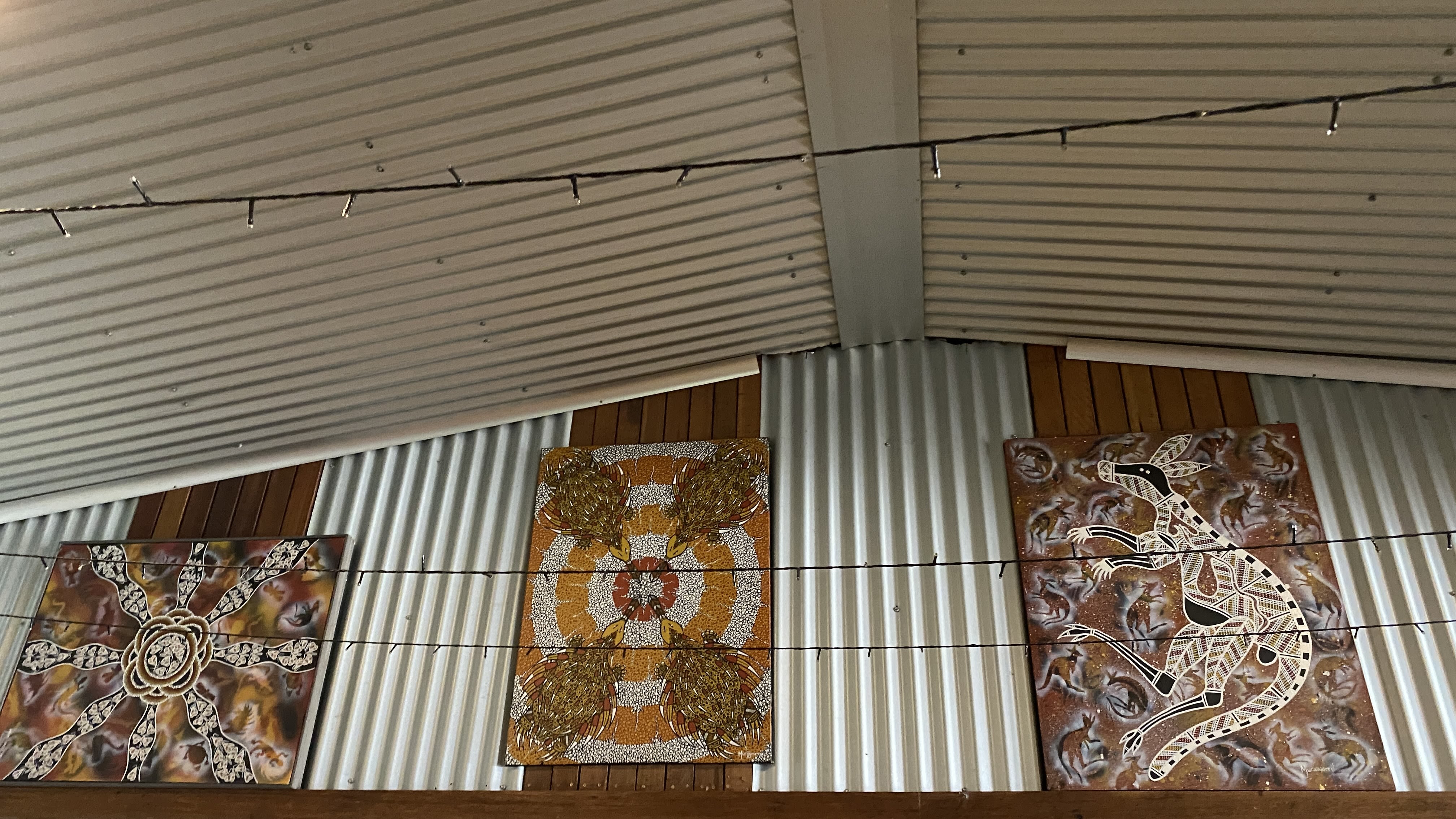 A set of three Aboriginal Australian dot paintings, hanging on a tin and wooden wall.
