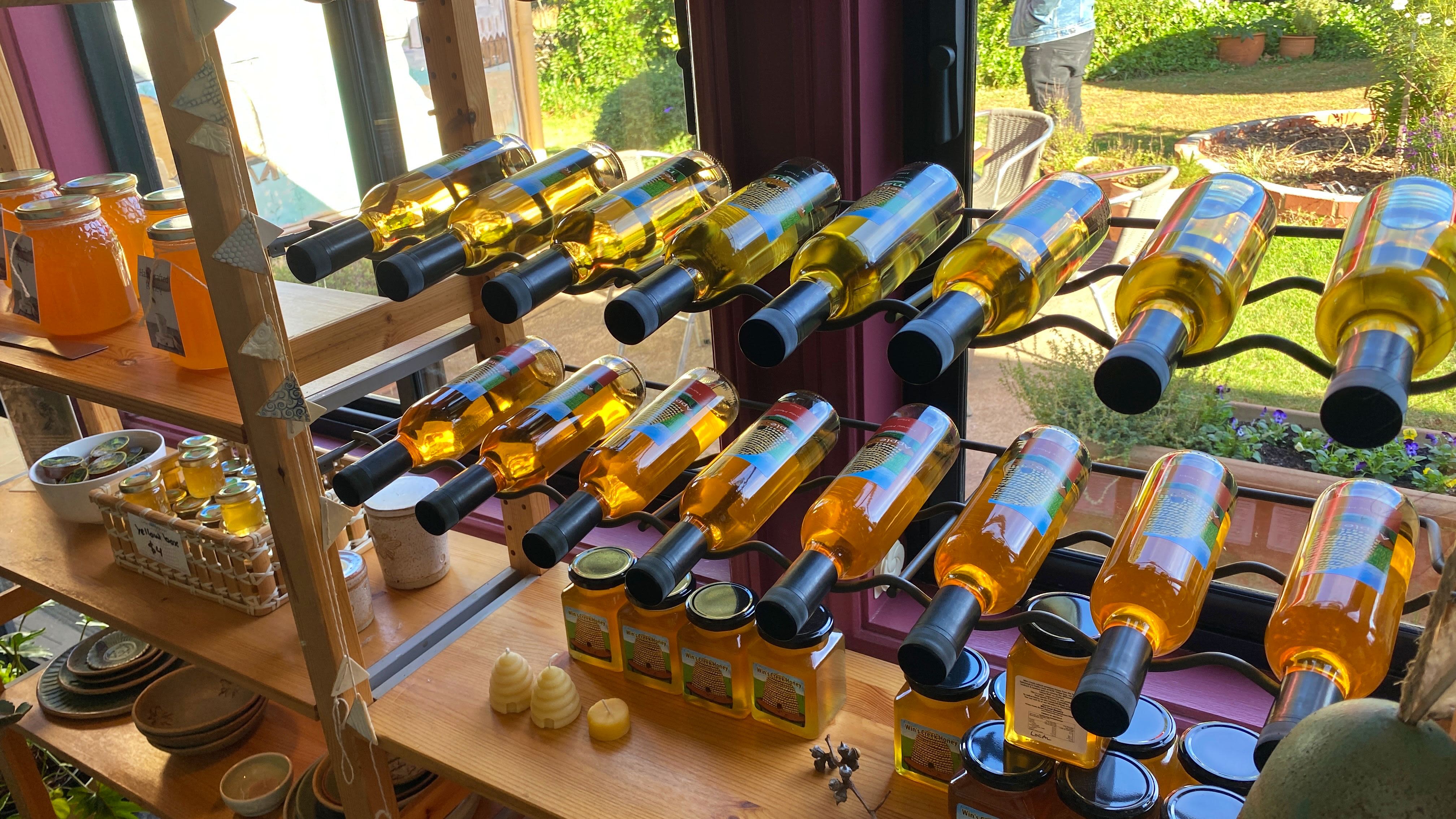 Two rows of mead bottles sit in front of a window. Next to them and below are several jars of honey.