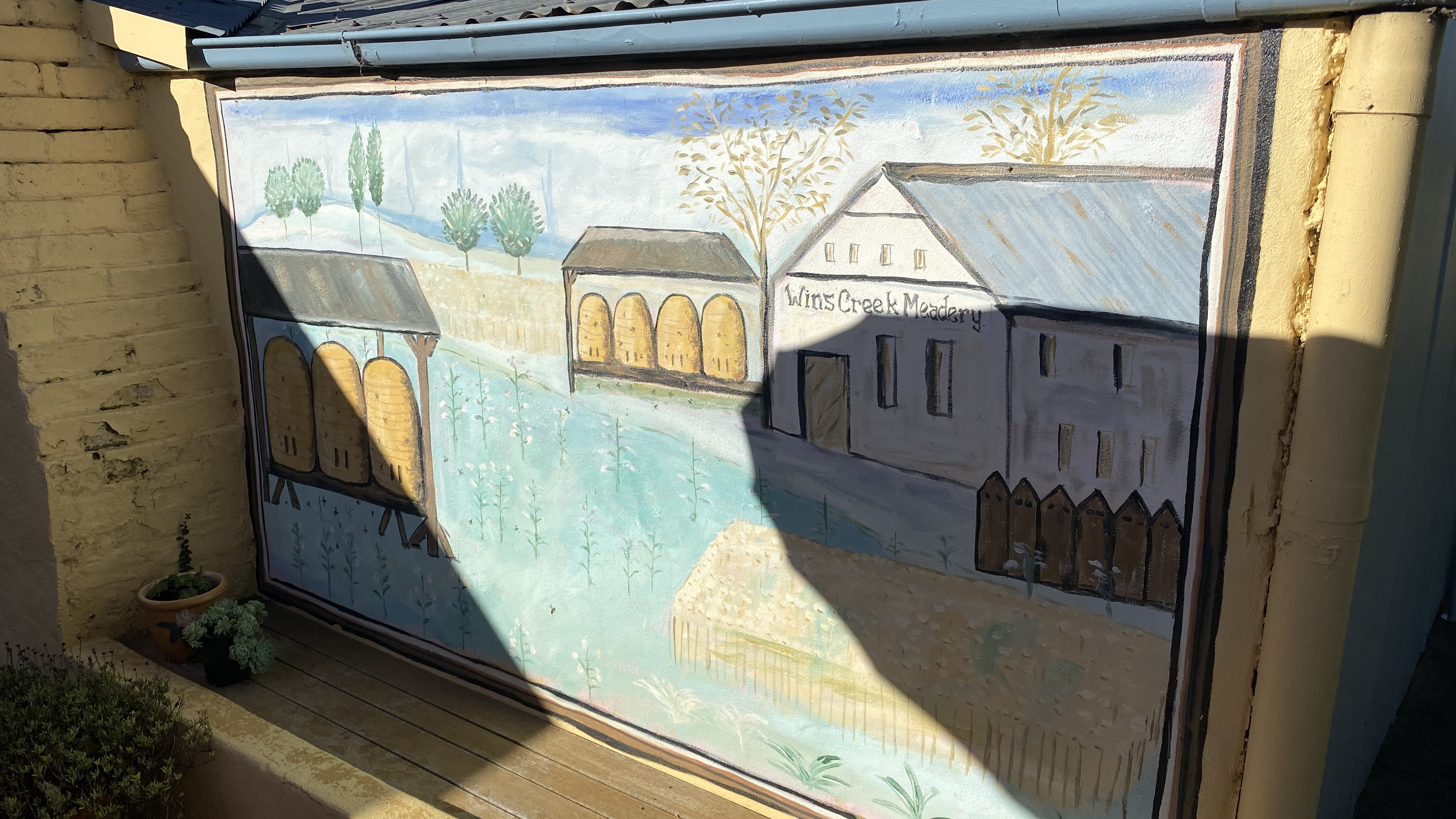 A wall mural depicting a shed and a collection of barns, the text reads "Wins Creek Meadery".