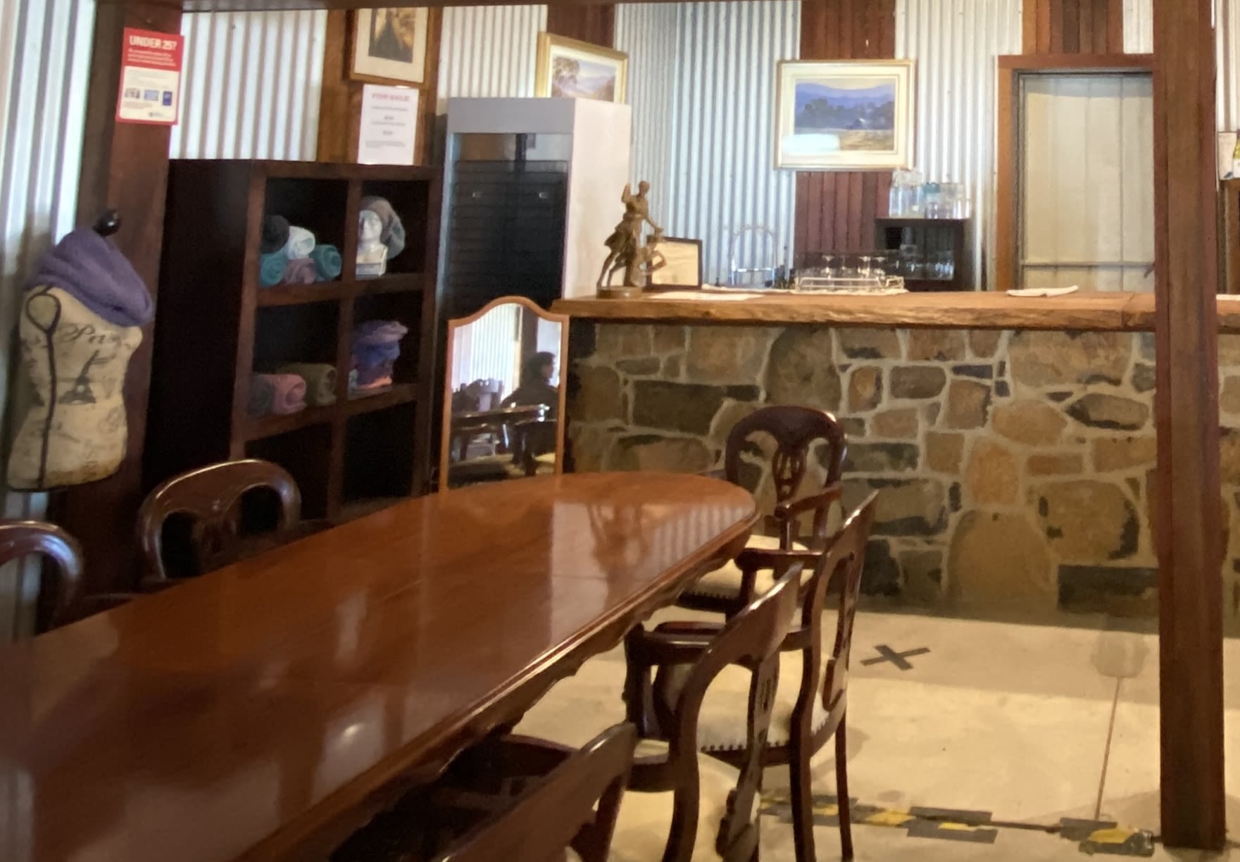 A fashion mannequin sits in the corer of a bookshelf, table, and mirror, sitting by the bar. The mannequin has a scarf around it's neck