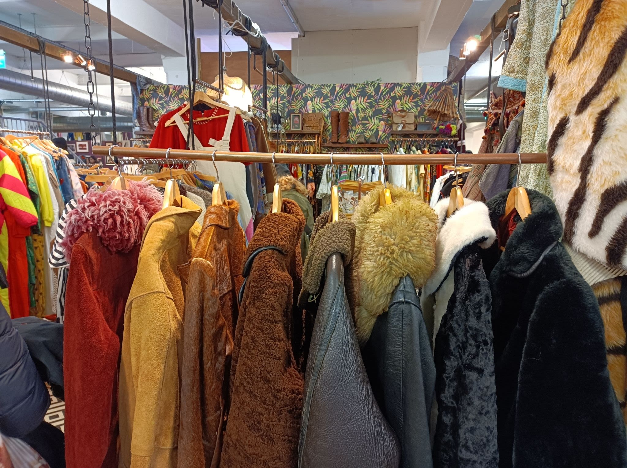 A rack of leather and fur-collared coats in red, brown and black, with a vintage clothing stalls in the background.