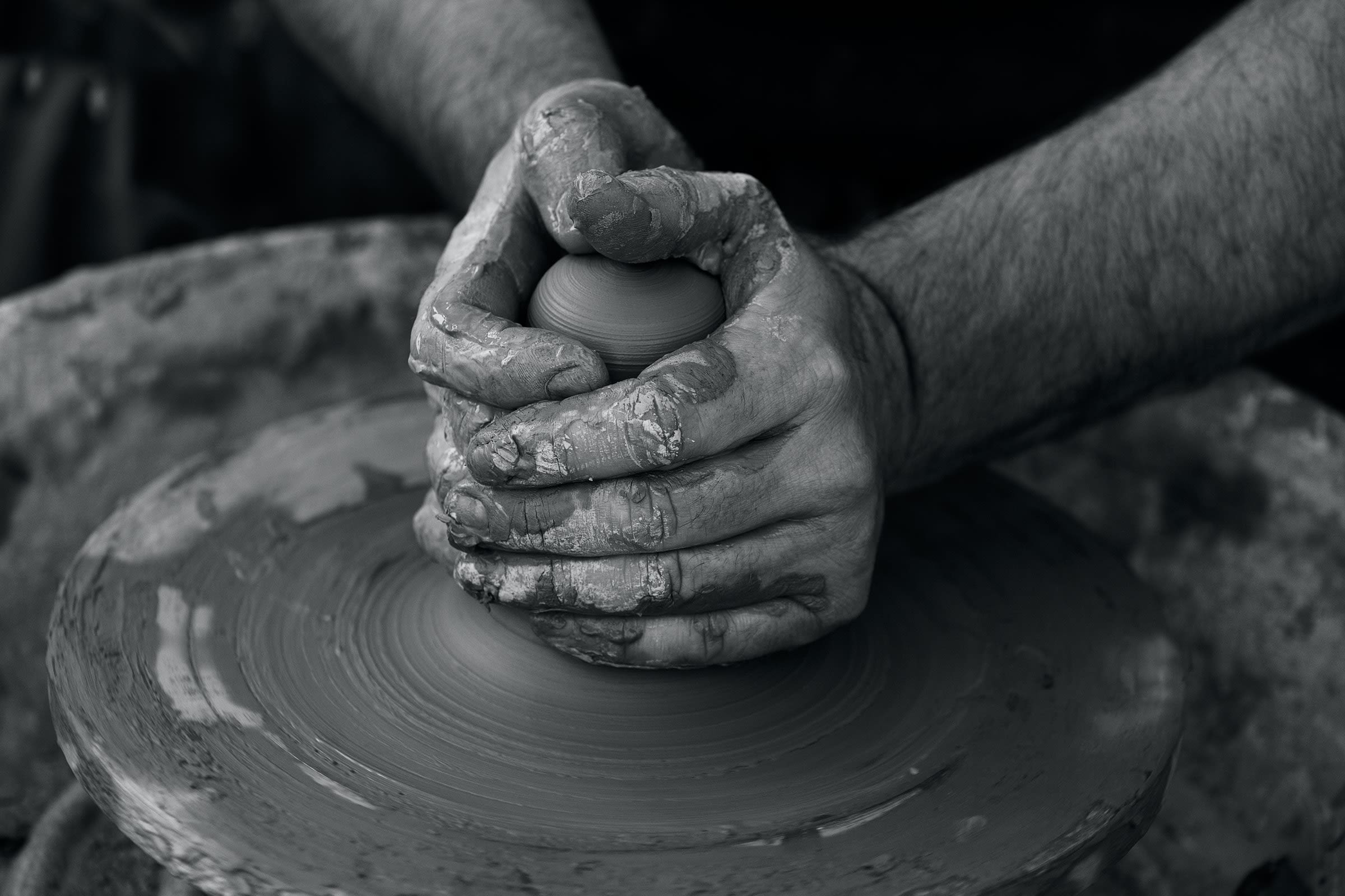 A black and white image of hands creating pottery on a wheel