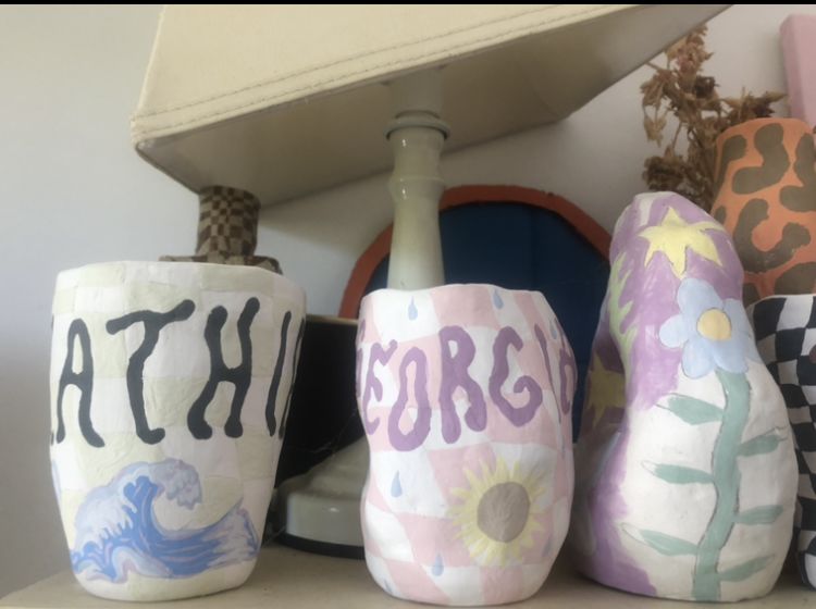 Colourful pink, purple vases on shelf. With stars and sunflowers on them